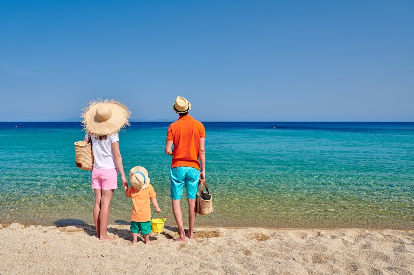 Familie steht am Sandstrand und blickt auf das Meer, Nähe Kokkini Hani