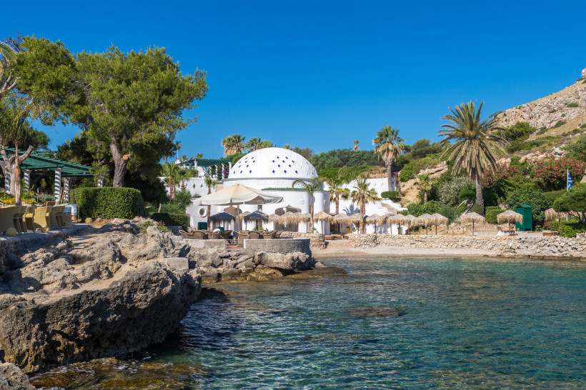 Weiße Kuppelarchitektur an felsiger Küste mit Palmen und klarem Meer auf Rhodos