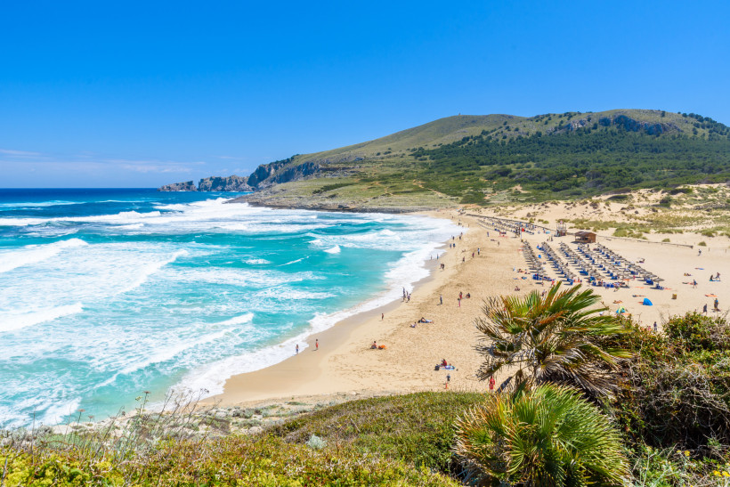 Blick über den Sandstrand von Cala Mesquida mit türkisfarbenem Meer, Brandung und Dünenlandschaft