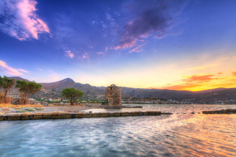 Olous: Küstenansicht mit steinernem Turm bei Sonnenuntergang Sonnenuntergang an der Küste von Olous mit steinernem Turm im Wasser und Bergen im Hintergrund
