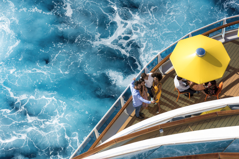 Costa Diadema: Blick auf das Außendeck mit Sonnenschirm und Meer Oberdeck der Costa Diadema mit gelbem Sonnenschirm und Personen am Geländer über blauem Meerwasser