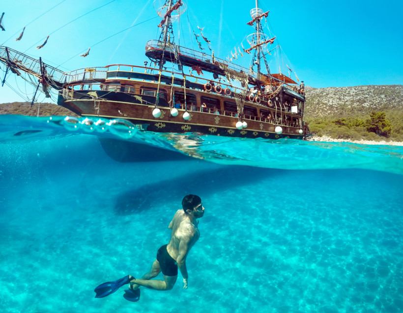 Schnorchler im kristallklaren Wasser unter einem Ausflugsboot an der türkischen Ägäis, Erlebnisferien mit Baden und Meer