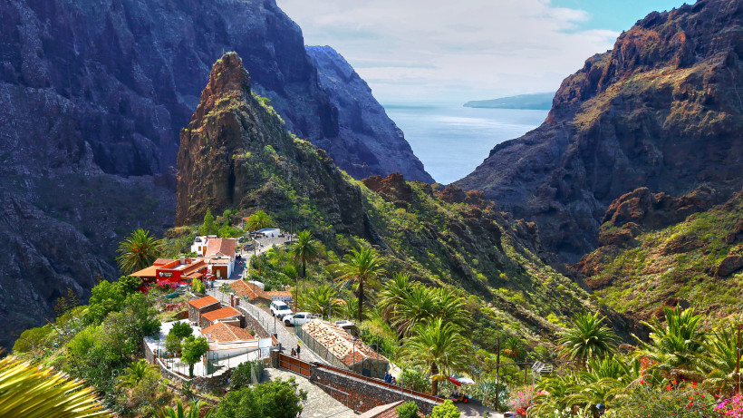 Blick auf das Bergdorf Masca auf Teneriffa mit Palmen, Felsen und Meer im Hintergrund