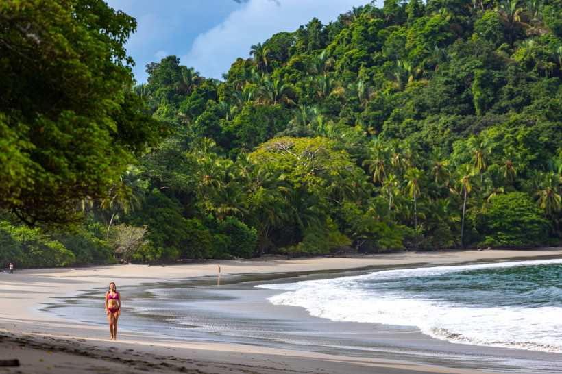 Strandurlaub in Costa Rica Frau spaziert am ruhigen tropischen Sandstrand entlang, umgeben von üppigem grünen Regenwald