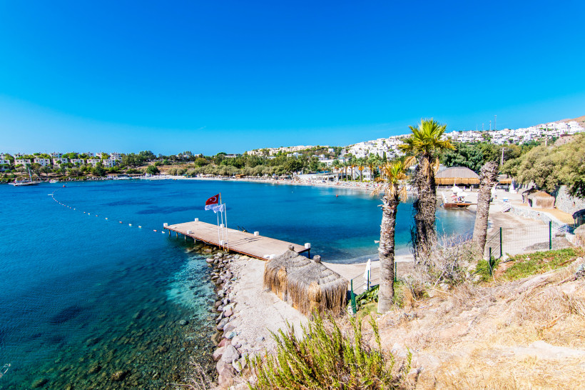 Ruhige Badebucht mit Holzsteg, Palmen, Sonnenschirmen und klarem türkisfarbenem Meer
