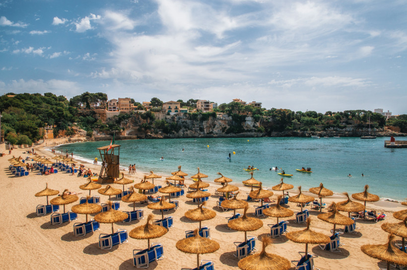 Porto Cristo, Mallorca Strand von Cala Marçal auf Mallorca mit Strohschirmen, Sonnenliegen und Badegästen in einer geschützten Bucht