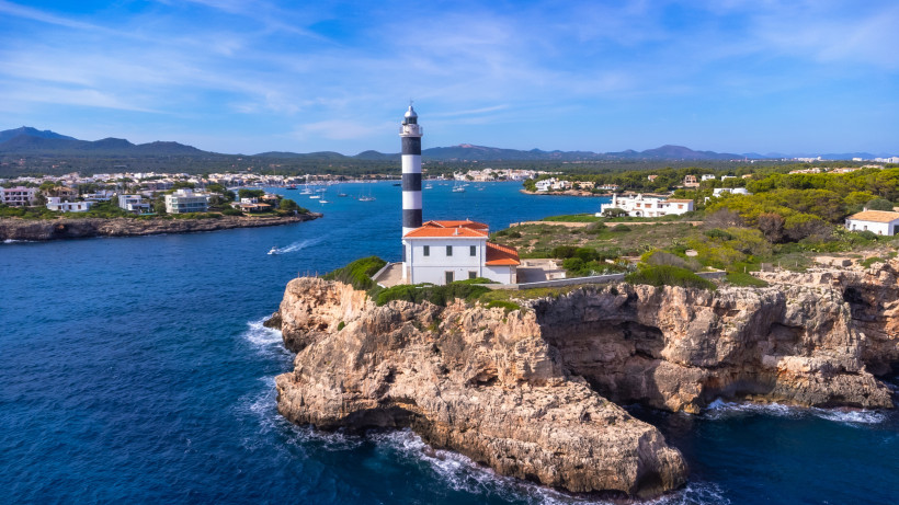 Leuchtturm Far de Portocolom auf einer Felsklippe an der Einfahrt zur Bucht von Portocolom