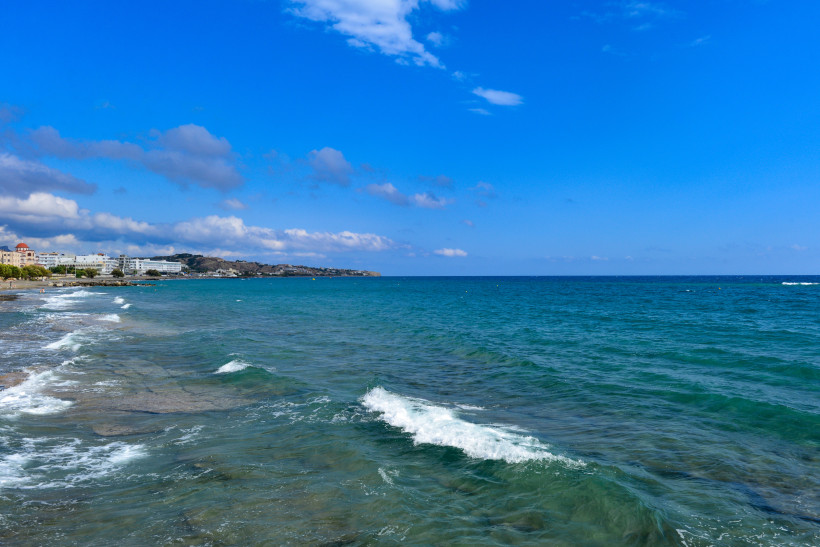 Küstenabschnitt am Strand von Ierapetra mit flachem Meer, kleinen Wellen und Wolken am blauen Himmel