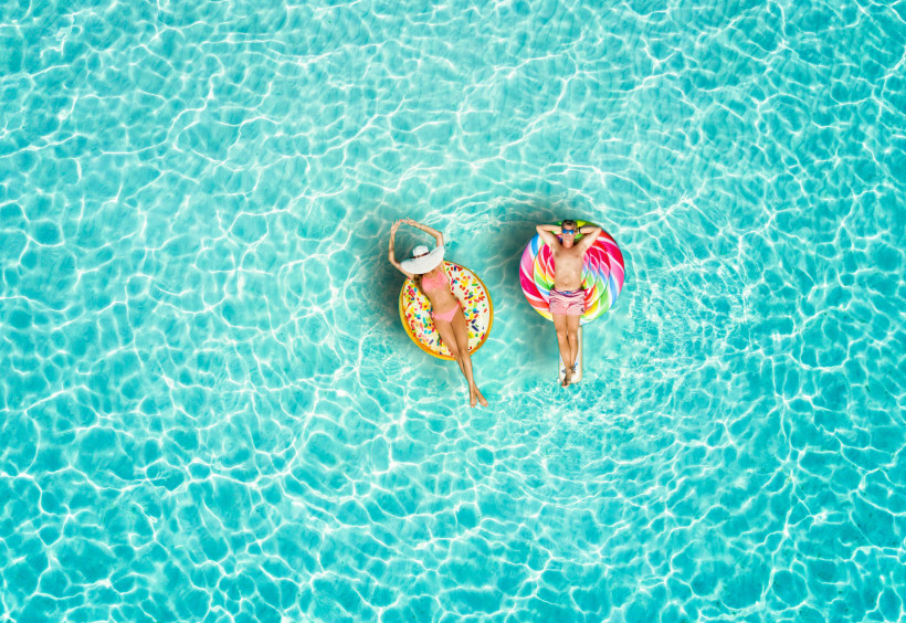 Malediven Ein Paar genießt die Sonne auf farbenfrohen Schwimmreifen im türkisblauen Wasser. Die perfekte Szene für pure Entspannung und sommerliche Urlaubsstimmung.