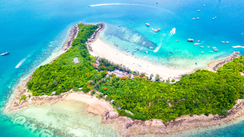 Luftaufnahme einer tropischen Insel mit weißem Sandstrand und türkisfarbenem Wasser bei Pattaya Luftaufnahme einer grünen tropischen Insel mit weißem Sandstrand, Booten und klarem türkisfarbenem Wasser bei Pattaya in Thailand
