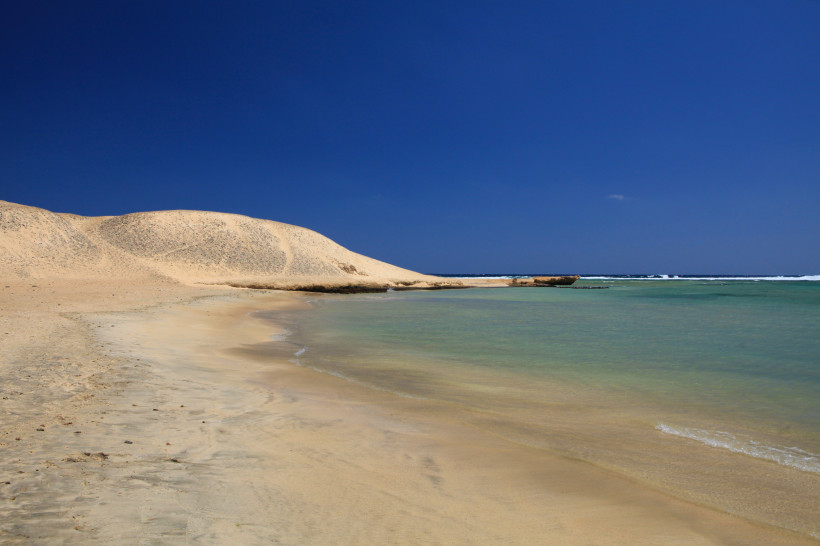 Ruhige Bucht in Marsa Mubarak mit hellen Sanddünen, flachem Wasser und tiefblauem Himmel.
