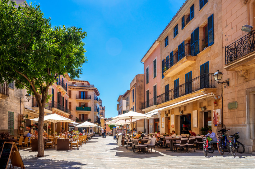 Belebte Altstadtgasse von Alcúdia mit Straßencafés, Natursteinfassaden und mediterraner Atmosphäre