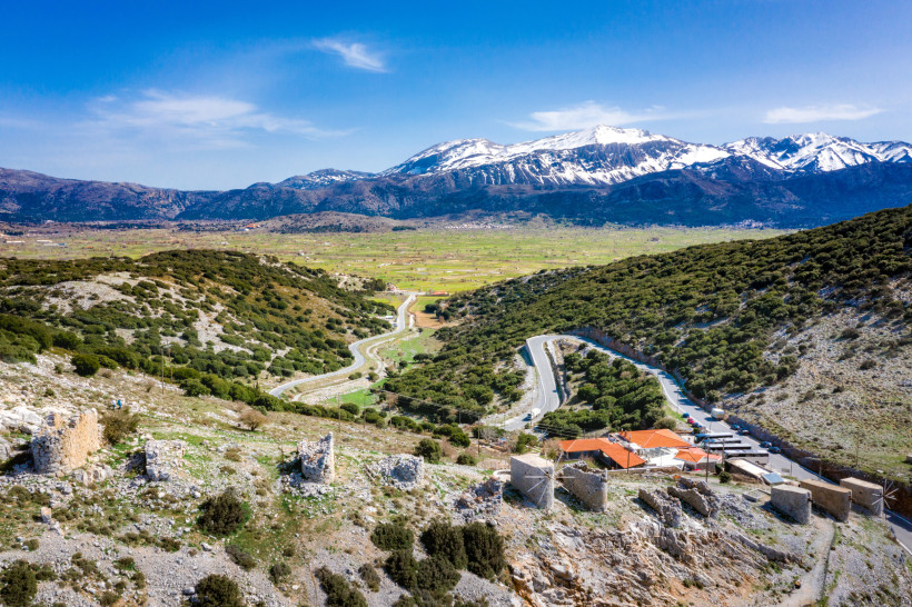 Lasithi-Hochebene auf Kreta mit Serpentinenstraße und Bergpanorama Blick über die Lasithi-Hochebene mit Serpentinenstraße und schneebedeckten Bergen im Hintergrund