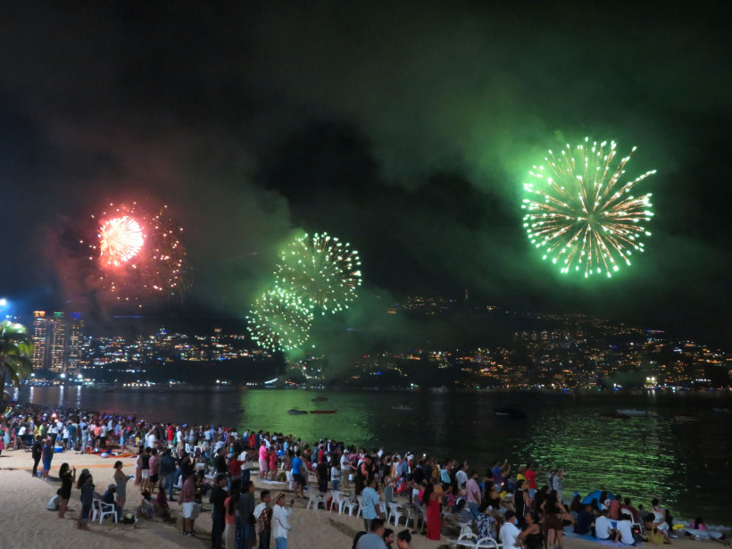 Jahreswechsel im Mexiko Menschenmenge am Sandstrand in Acapulco, die ein großes Feuerwerk in Grün und Rot über der Bucht bei Nacht beobachtet