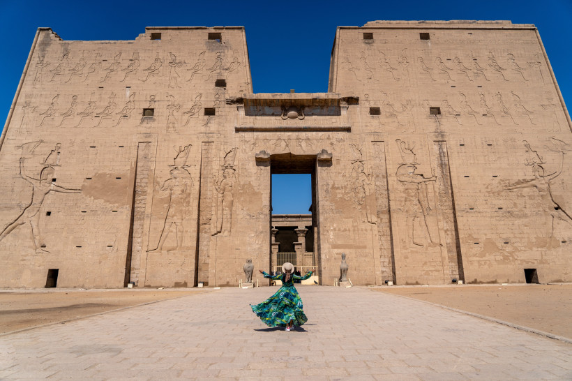 Ägypten - El Gouna Frau in farbigem Kleid steht vor dem monumentalen Eingang eines altägyptischen Tempels mit kunstvoll gemeißelten Reliefs an der Fassade.
