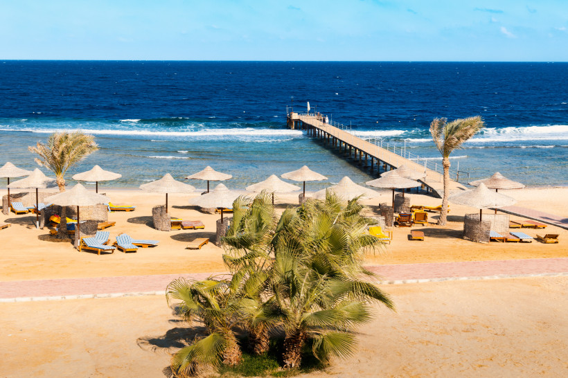 Strand von Marsa Alam mit Sonnenschirmen, Sonnenliegen und langem Steg ins Rote Meer