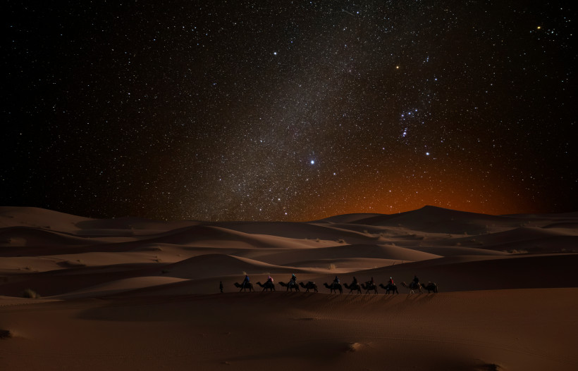 Kameltour durch die sandige Wüstenlandschaft bei Nacht unter einem leuchtenden Sternenhimmel