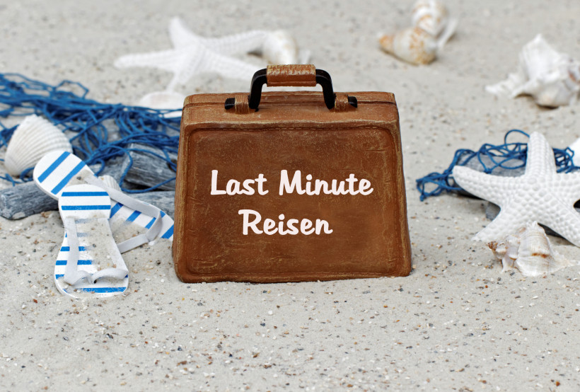 Last Minute Reisen – Koffer im Sand mit Stranddeko als Symbol für spontane Urlaubsangebote