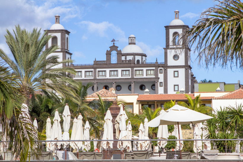 Gebäude im Villa-del-Conde-Bereich mit weißen Kuppeln und Türmen, Palmen und geschlossenen Sonnenschirmen im Vordergrund