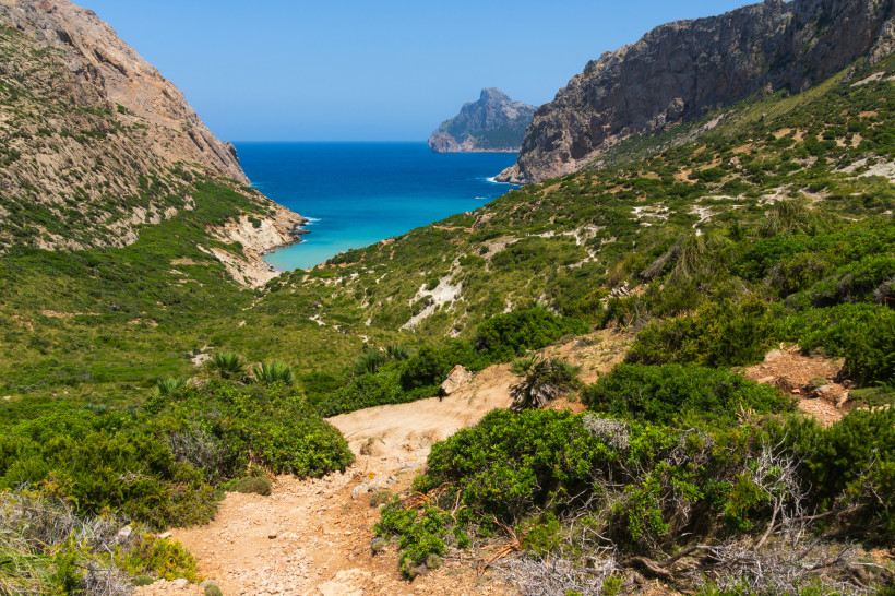 Blick auf Cala Boquer mit türkisblauer Bucht zwischen felsigen Hängen und mediterraner Vegetation