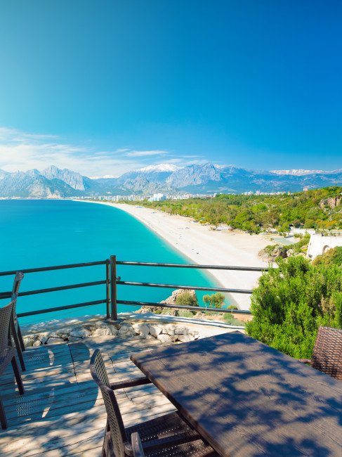 Konyaaltı-Strand in Antalya, Türkei: ruhiges türkisfarbenes Mittelmeer, blauer Himmel und üppiges Grün. 