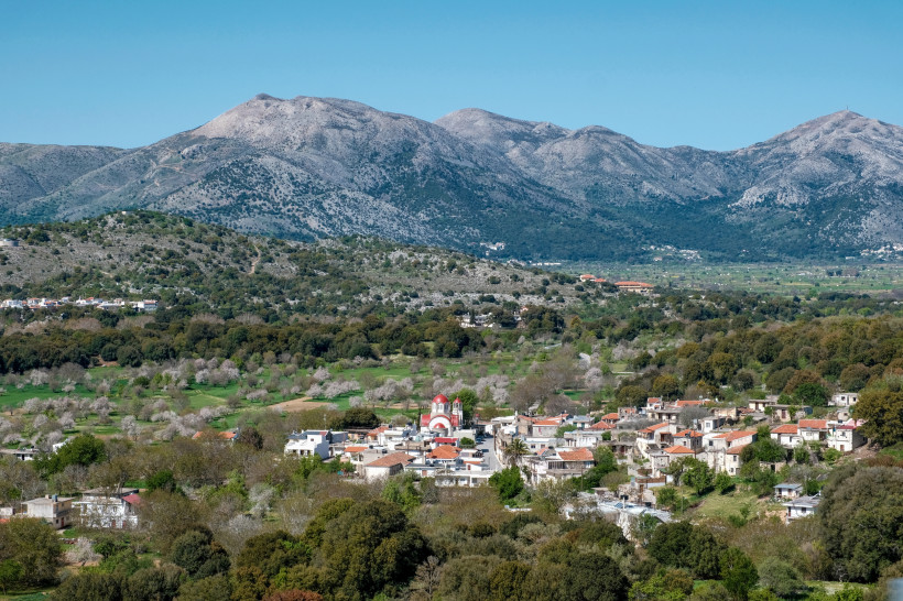 Lassithi-Hochebene auf Kreta mit Dorf im Tal und Bergen im Hintergrund Blick über die Lassithi-Hochebene mit Dorf und Kirche vor einem Gebirgszug
