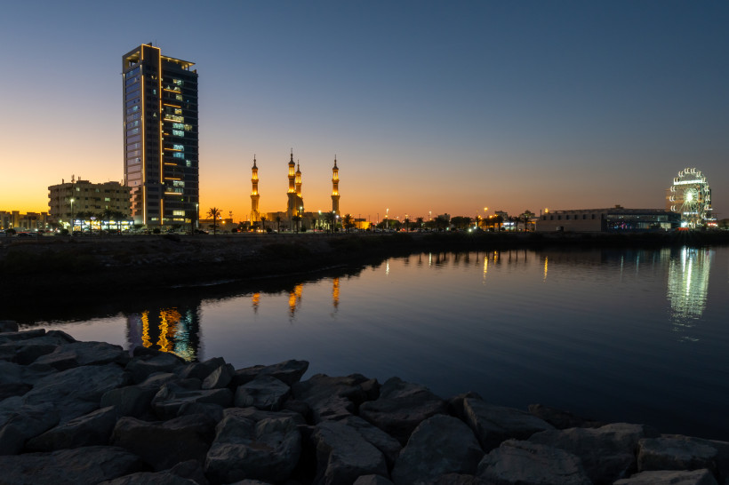 Skyline von Ras Al Khaimah bei Sonnenuntergang mit Moschee, Riesenrad und Wasserreflexionen an der Corniche.
