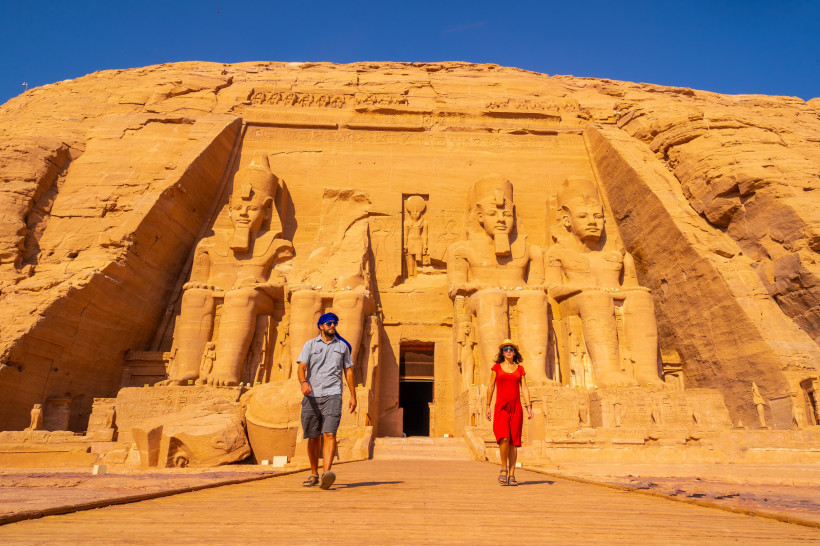 Das Bild zeigt den imposanten Eingangsbereich des Großen Tempels von Abu Simbel in Südägypten. Vier riesige, sitzende Statuen von Pharao Ramses II. sind direkt in den Sandsteinfelsen gehauen. Zwischen den Statuen befindet sich der Tempeleingang. Zwei Tour
