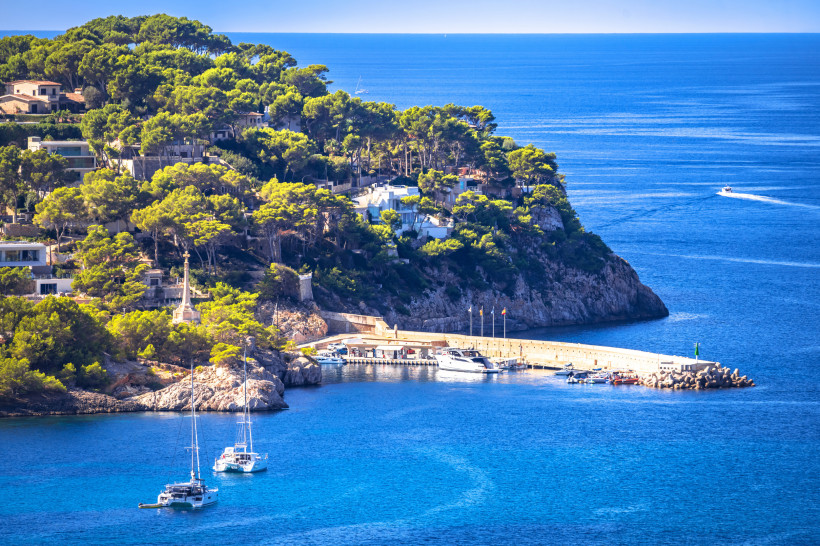 Cruz de la Conquista an der Küste mit Kiefernwald, Hafenmole und Segelbooten im Meer