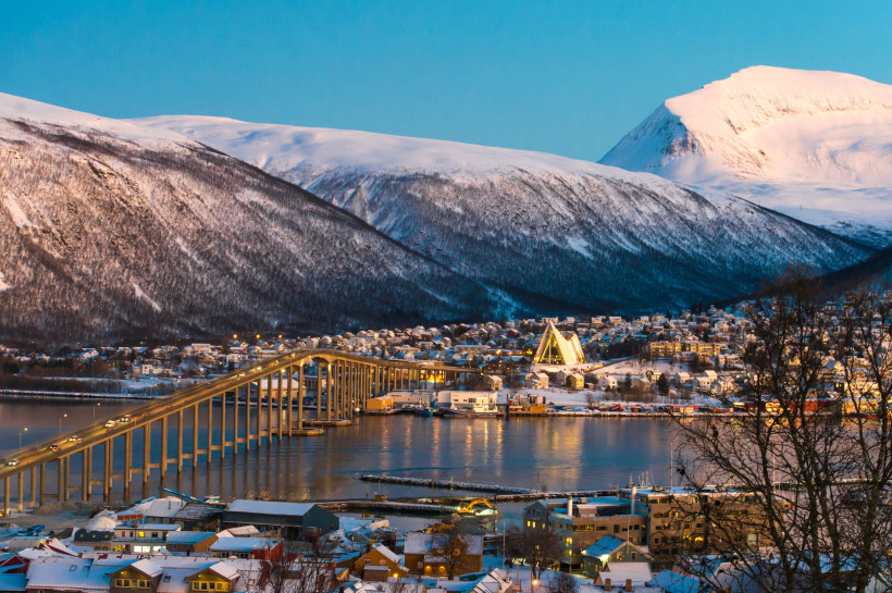Tromsø mit Eismeerkathedrale und Brücke vor schneebedeckten Bergen Blick auf Tromsø mit Eismeerkathedrale, Brücke und schneebedeckten Bergen im Winter