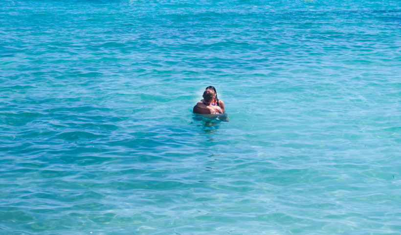 Paar umarmt sich im türkisblauen, glasklaren Meer vor der Küste Mallorcas, ruhige Wasseroberfläche und sonnige Urlaubsatmosphäre