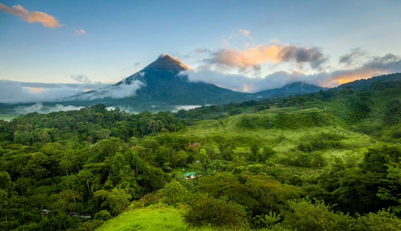 Costa Rica, Regenzeit Üppig grüne tropische Landschaft mit dichtem Regenwald und dem Vulkan Arenal im Hintergrund, teilweise von Wolken umhüllt, bei Sonnenaufgang