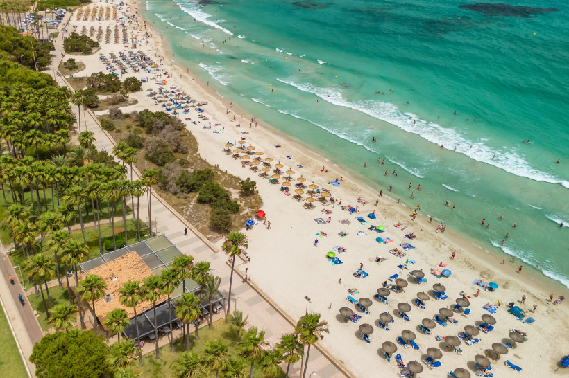 Luftaufnahme der Playa de Sa Coma mit Sandstrand, Sonnenschirmen und Badenden im türkisfarbenen Meer