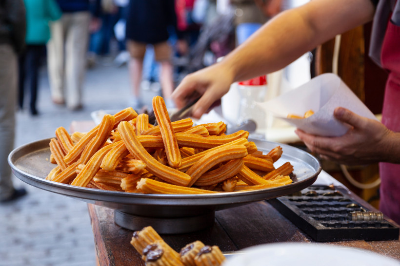 Frische Churros auf einem großen Tablett, während ein Verkäufer sie in eine Tüte verpackt