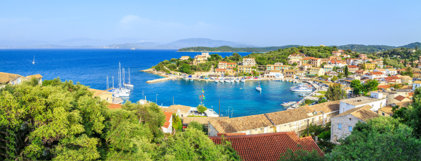 Panoramablick auf die Bucht von Kassiopi mit Segelbooten und bunten Häusern am Wasser
