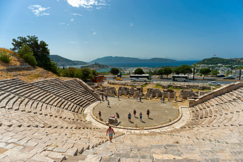 Antikes Amphitheater in Bodrum mit steinernen Sitzreihen, Besuchern und Blick auf den Hafen und das Meer im Hintergrund