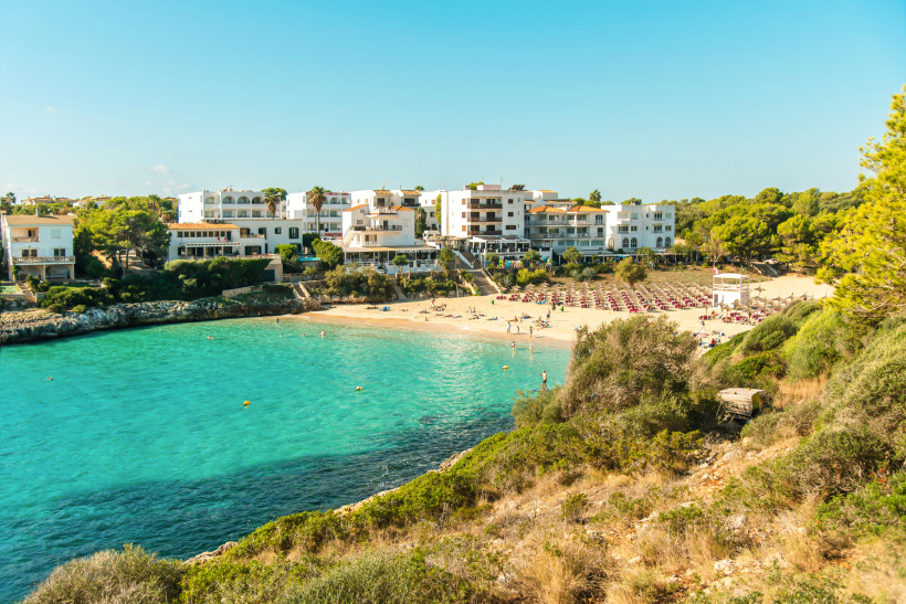 Bucht Cala Marçal bei Portocolom mit Sandstrand, Sonnenschirmen und Hotelgebäuden am Ufer