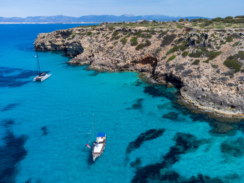Boote vor der Felsküste am Cap Enderrocat mit türkisfarbenem Wasser