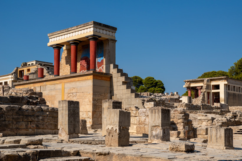 Palast von Knossos auf Kreta, Ruinen mit rekonstruierten Säulen und Wandmalerei Ruinenanlage des Palasts von Knossos mit rekonstruiertem Gebäudeteil und roten Säulen unter blauem Himmel