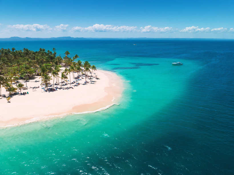Dominikanische Republik Traumstrand der Dominikanischen Republik mit weißem Sand, Palmen und türkisfarbenem Wasser – ein Boot liegt vor der Küste.