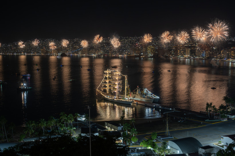 Jahreswechsel im Mexiko Panorama-Nachtaufnahme der Bucht von Acapulco mit spektakulärem Feuerwerk am Himmel und einem festlich beleuchteten Segelschiff im Hafen
