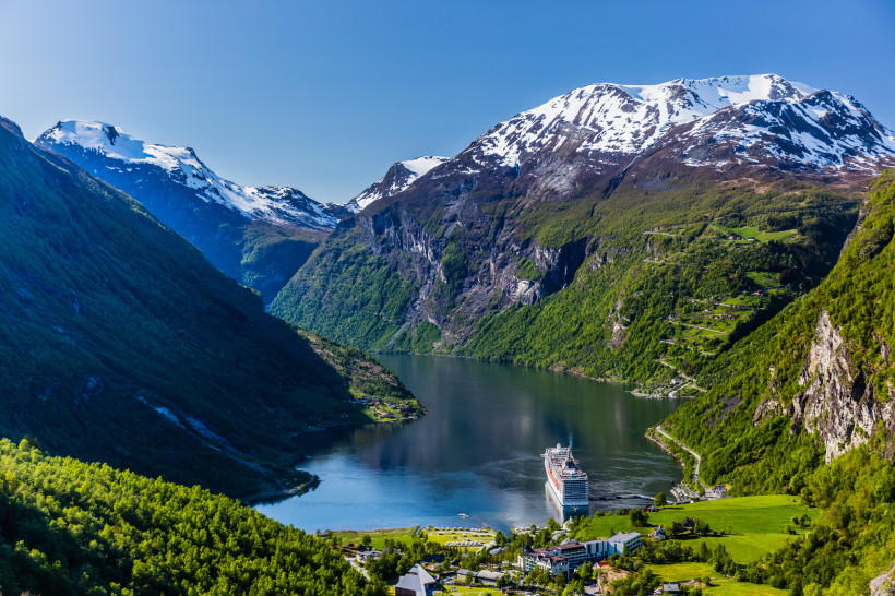 Blick über den Geirangerfjord mit Kreuzfahrtschiff, grünen Berghängen und schneebedeckten Gipfeln