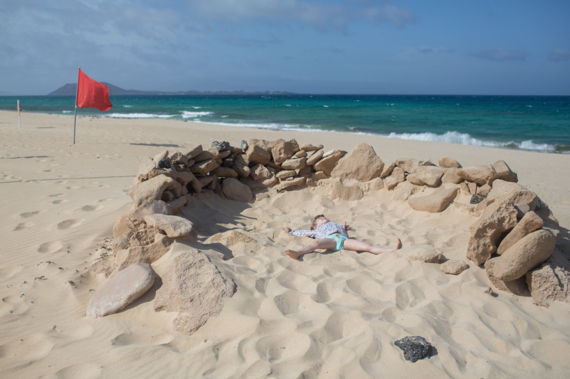 Steinkreis als Windschutz im Sand am Strand, rote Fahne und Meer im Hintergrund