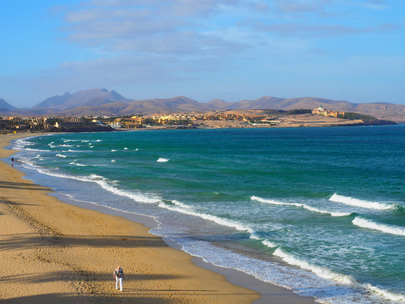 Küstenpanorama bei Costa Calma mit Sandstrand, Wellen und Bergen im Hintergrund