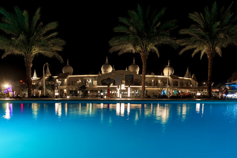 Beleuchtete Hotelanlage bei Nacht mit großem Pool im Vordergrund