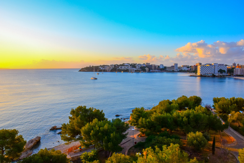 Blick über die Bucht von Palma Nova mit Küstenbebauung und Segelbooten bei Sonnenuntergang