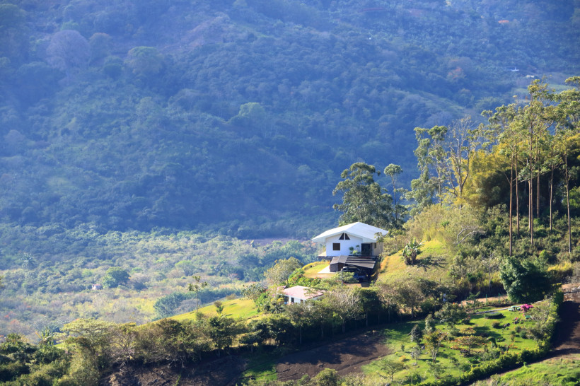 Haus in den Bergen des Valle Central Weißes Haus auf einem grünen Hügel im Valle Central in Costa Rica, umgeben von Bäumen und Bergpanorama