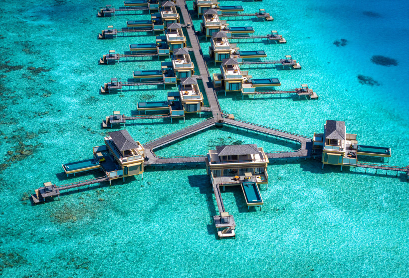 Luftaufnahme von Wasserbungalows mit Stegen über türkisfarbenem Wasser im Dhaalu-Atoll