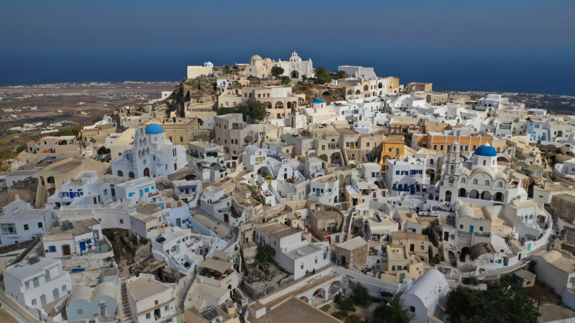Panoramablick auf Pyrgos, Santorini: verwinkelte Gassen, weiße Häuser und Kirchen mit blauen Kuppeln hoch über der Insel