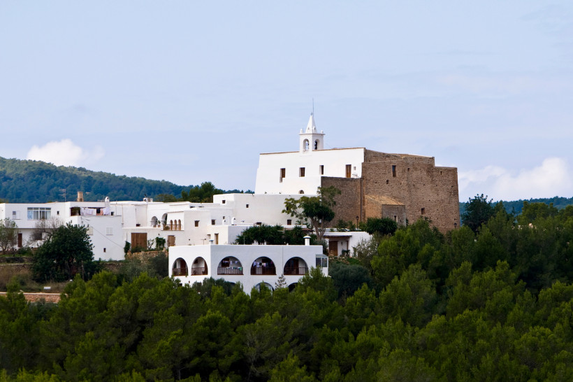 Ibiza - Sant Josep de sa Talaia Blick auf das Dorf Sant Josep de sa Talaia auf Ibiza mit weiß getünchten Häusern und der traditionellen Kirche, die sich über den grünen Kiefernwald erhebt.